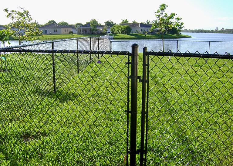 A Black Chain Link Fence With a Gate Overlooks a Tranquil Lake in Palm Beach County, FL.